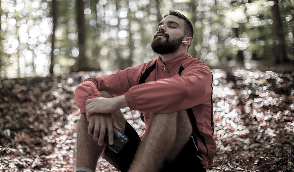 Foto: Eine Person sitzt auf dem Waldboden und entspannt